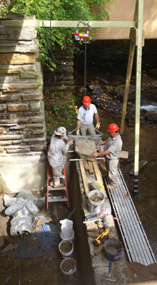 A team of Fallingwater’s preservation maintenance technicians resets large capstones following repairs to the wall of the plunge pool in 2017.