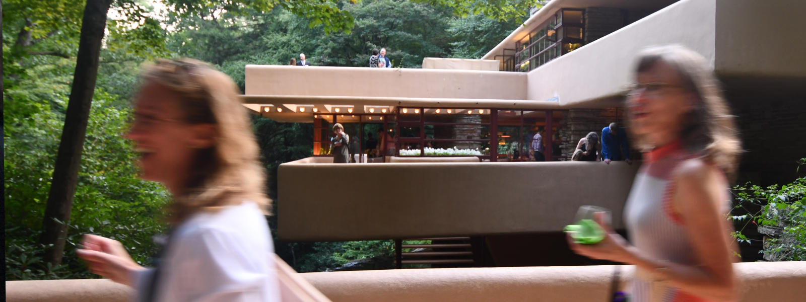 Photo of people walking on the bridge with the Fallingwater house behind them