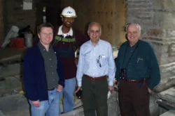 Four men (John Matteo, Jason Hughes, Bob Silman, Mario Suarez) stand between the exposed concrete floor beams during the post-tensioning preservation process in 2002.