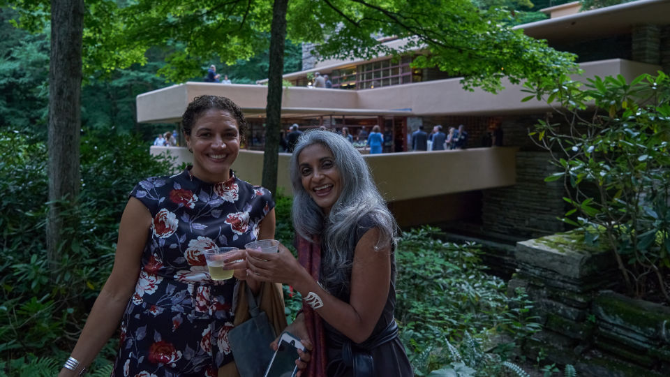 Two guest of the Fallingwater Soirée pose in front of a view of the southeast terrace of the house from across Bear Run.