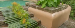 A decorative flower arrangement cascades down the stone steps of a pool atop a mat made of bamboo.