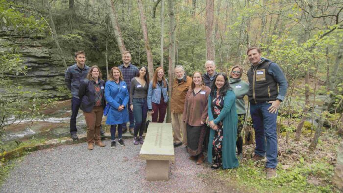 George Longenecker and many of his past interns pose at the stone bench along Bear Run that was dedicated in spring 2023 in recognition of his contributions to Fallingwater.