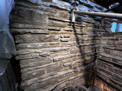 A brick wall has a series of small holes drilled into it. There is scaffolding and plastic surrounding the brick wall.